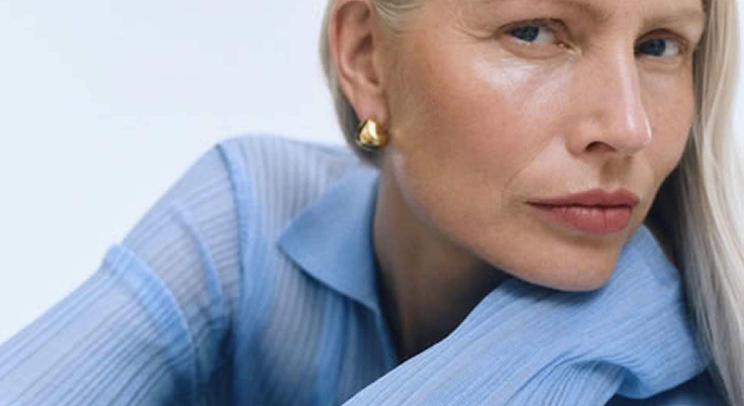 Woman wearing gold stud earrings and light blue ribbed blouse, minimalist style